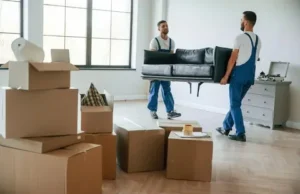 Movers carrying a sofa with boxes in a new apartment.